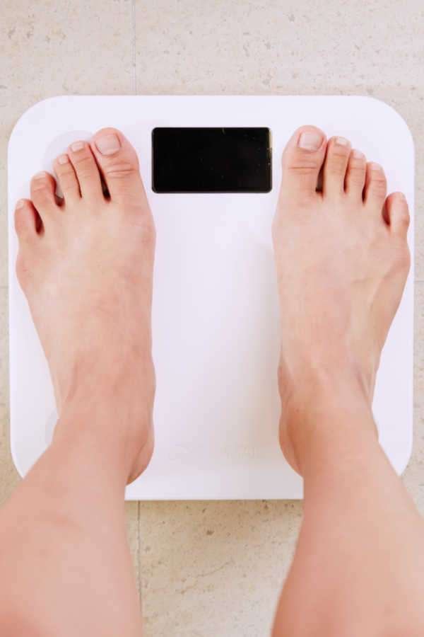 Person weighing themselves on a white scale. Do you have to lose weight before knee surgery?  New Knee for the New Year?  2 Major Reasons Not To Put Off Knee Replacement Surgery