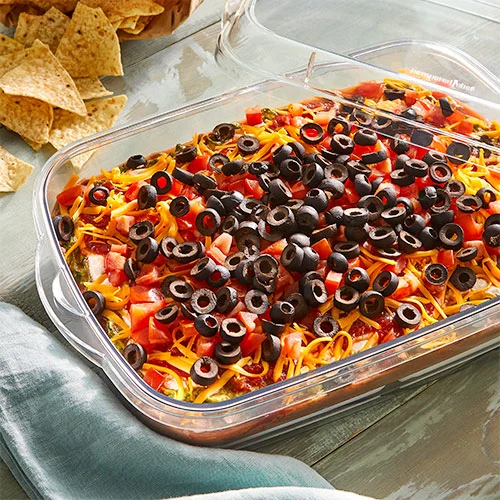 SEVEN-LAYER DIP inside of the rectangular cool n serve on a table with tortila chips 