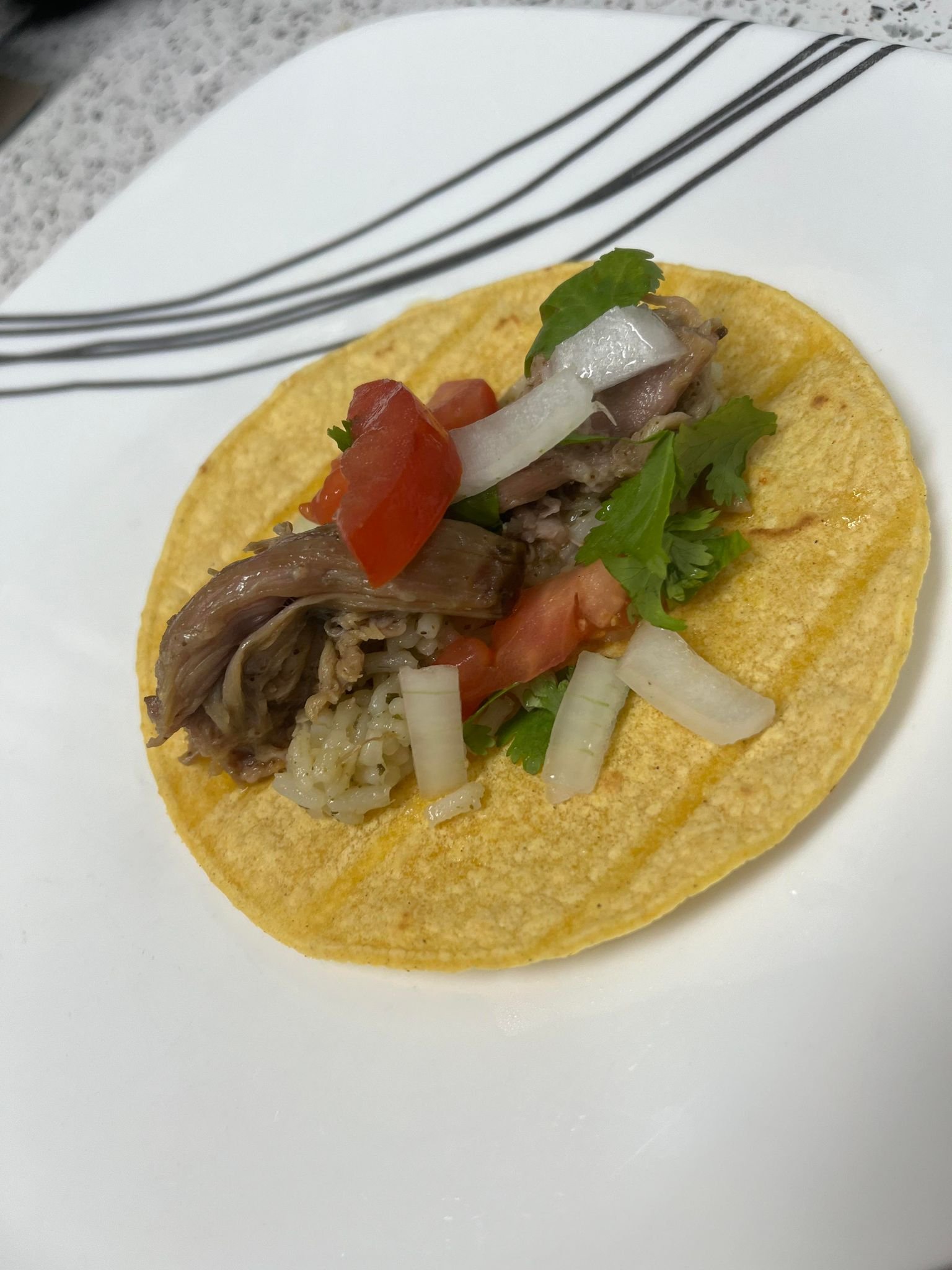 Slow cooker carnita with onion, cilantro, tomato, and lime rice on a tortila on a white plate